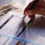 Stock image showing a woman’s hand filling in a postal ballot / voting form.